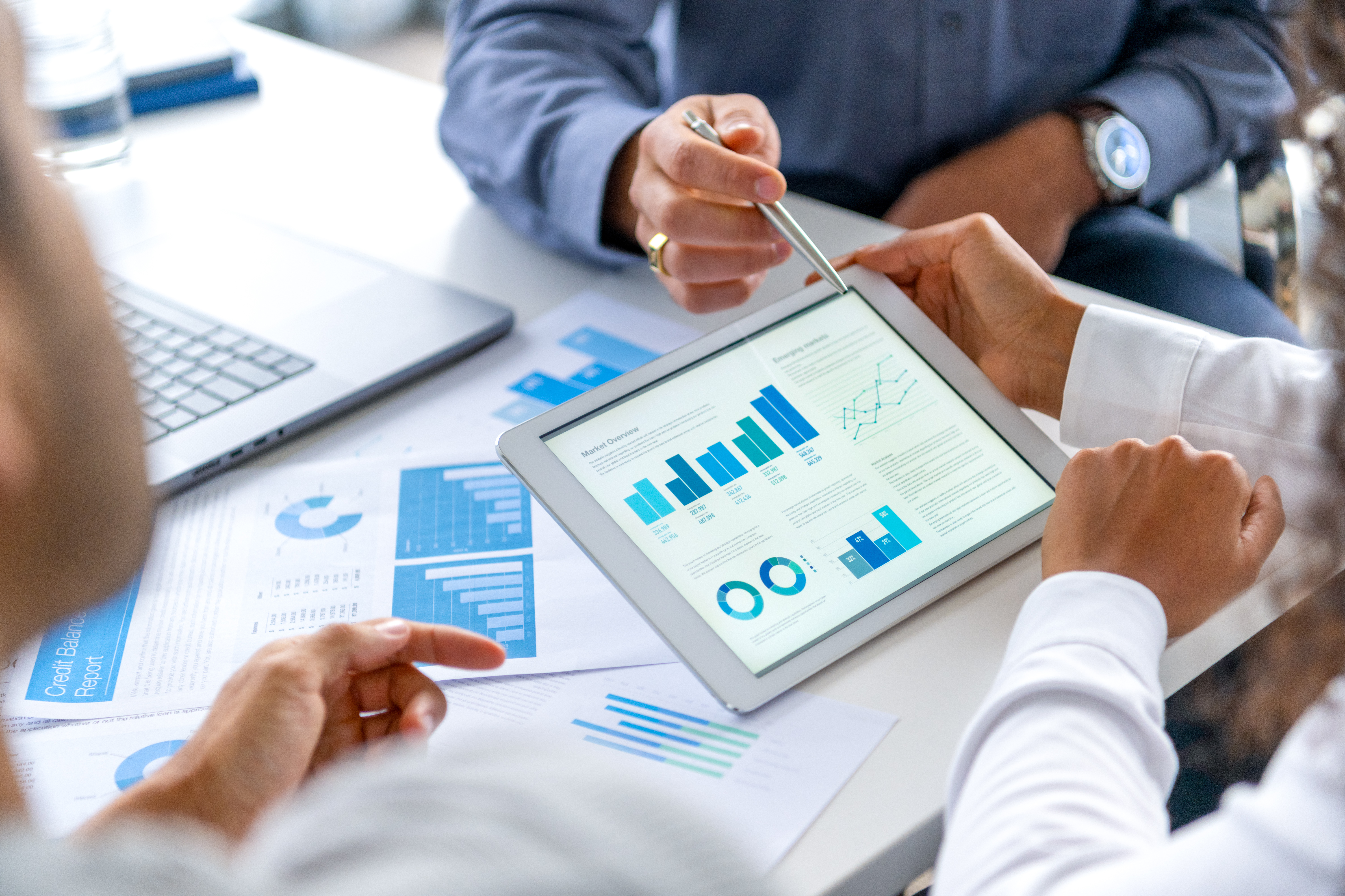 Business professionals reviewing market overview charts and graphs on a tablet during a meeting.
