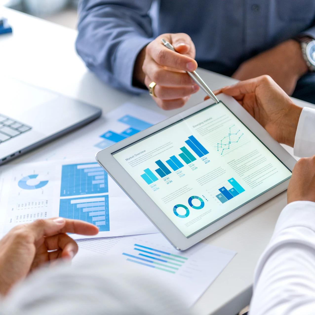 Business professionals reviewing market overview charts and graphs on a tablet during a meeting.