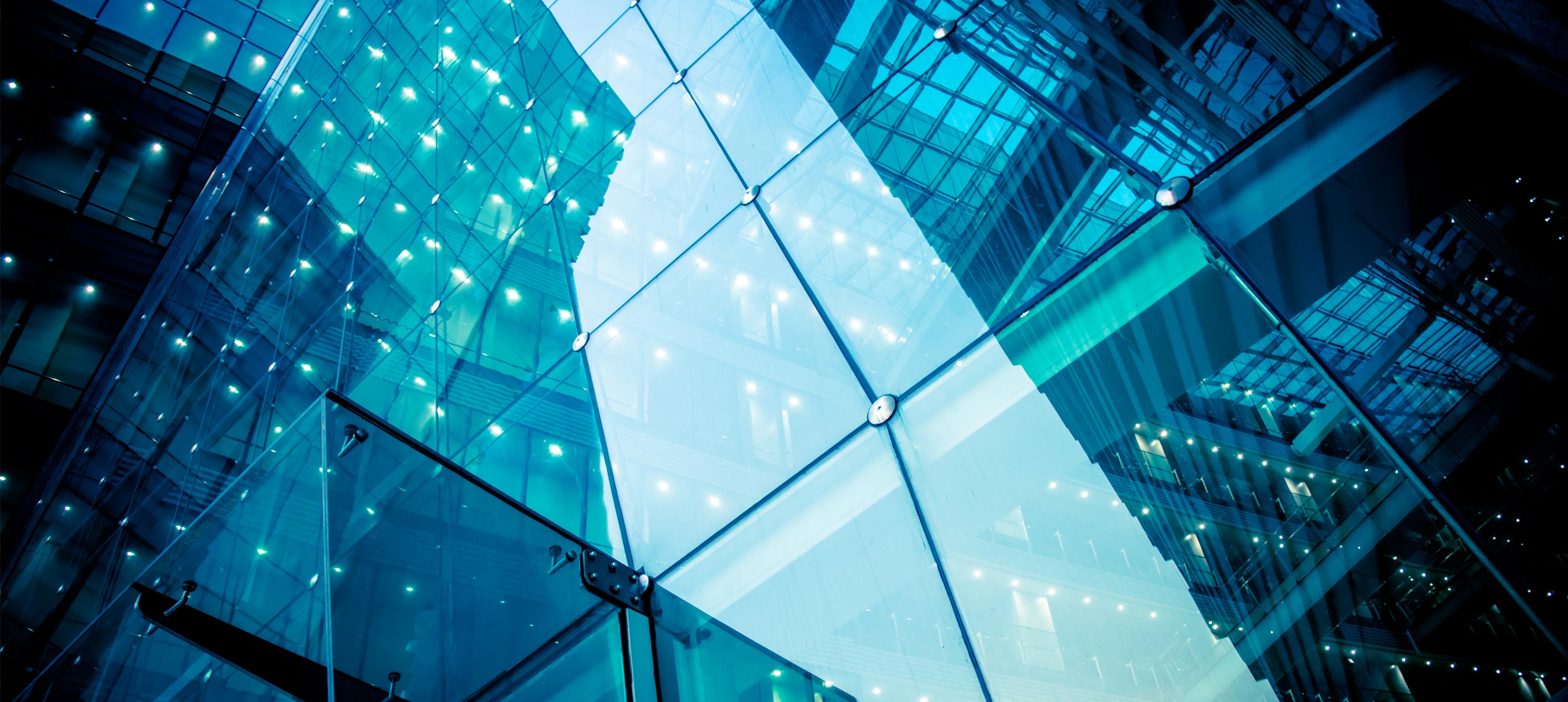 Looking up at a glass building with metal-fixed panels, blue-tinted and lit by rows of small white lights.