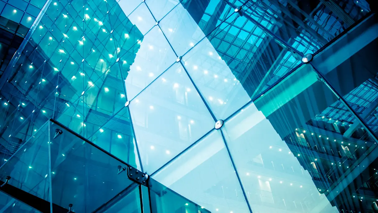 Looking up at a glass building with metal-fixed panels, blue-tinted and lit by rows of small white lights.