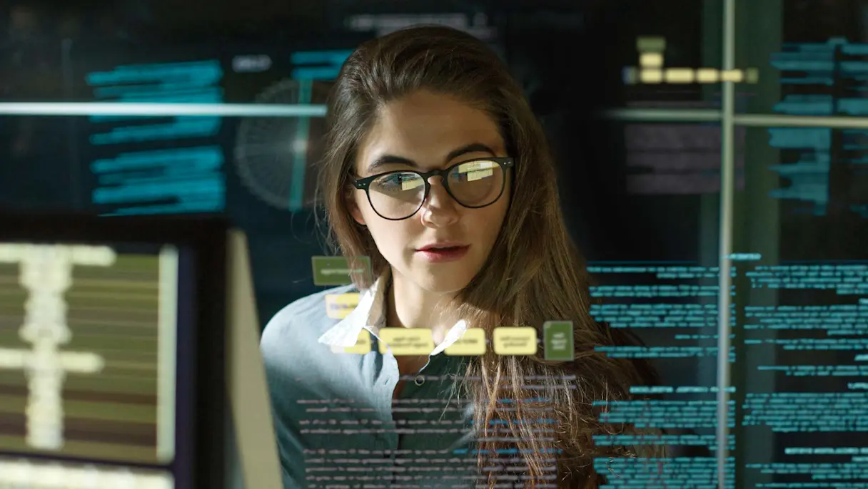 A professional woman wearing glasses analyzing digital data displays and charts on a transparent screen.
