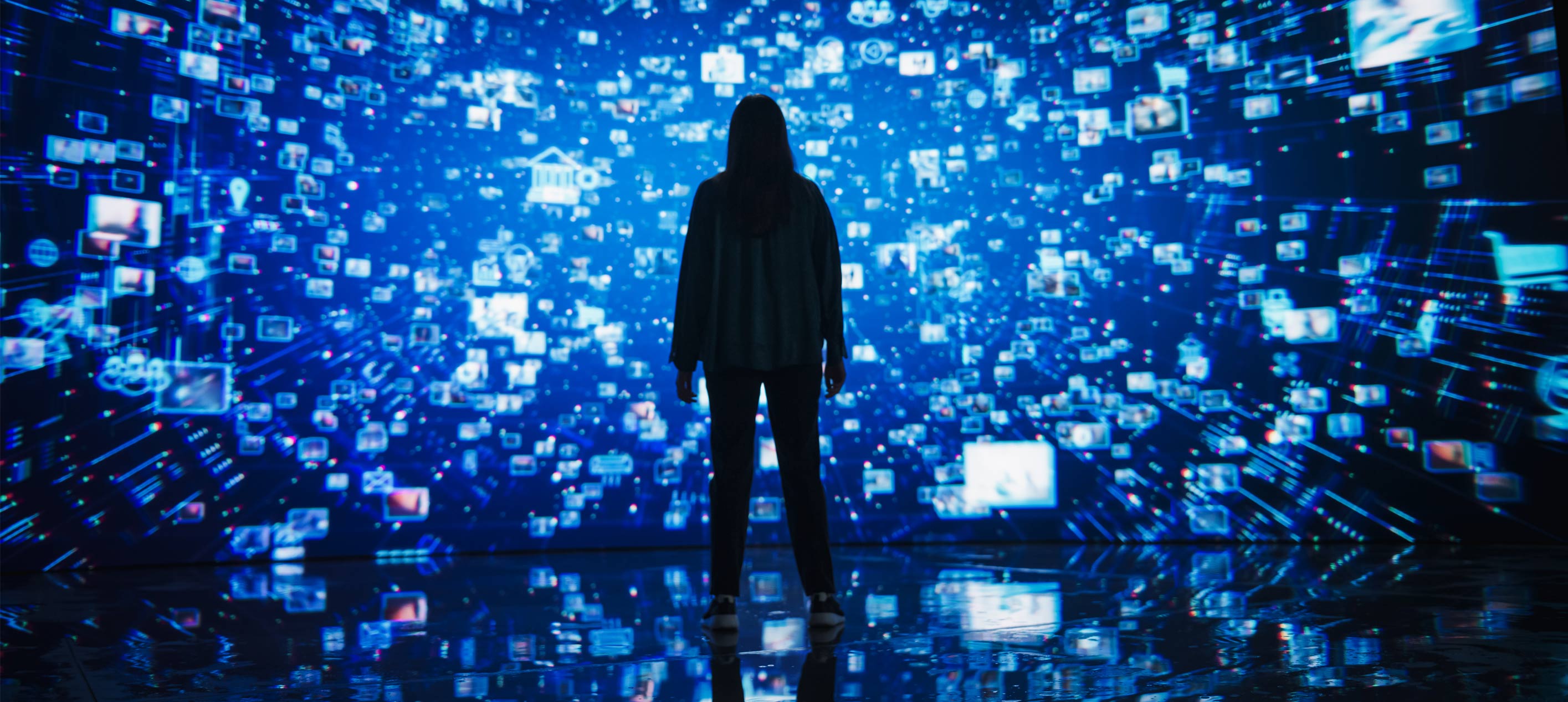 Silhouette of a person standing before an immersive digital wall covered in blue data icons and images.
