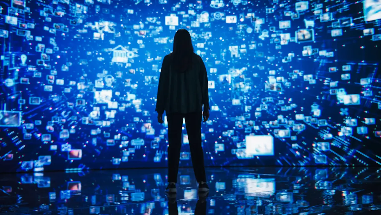 Silhouette of a person standing before an immersive digital wall covered in blue data icons and images.