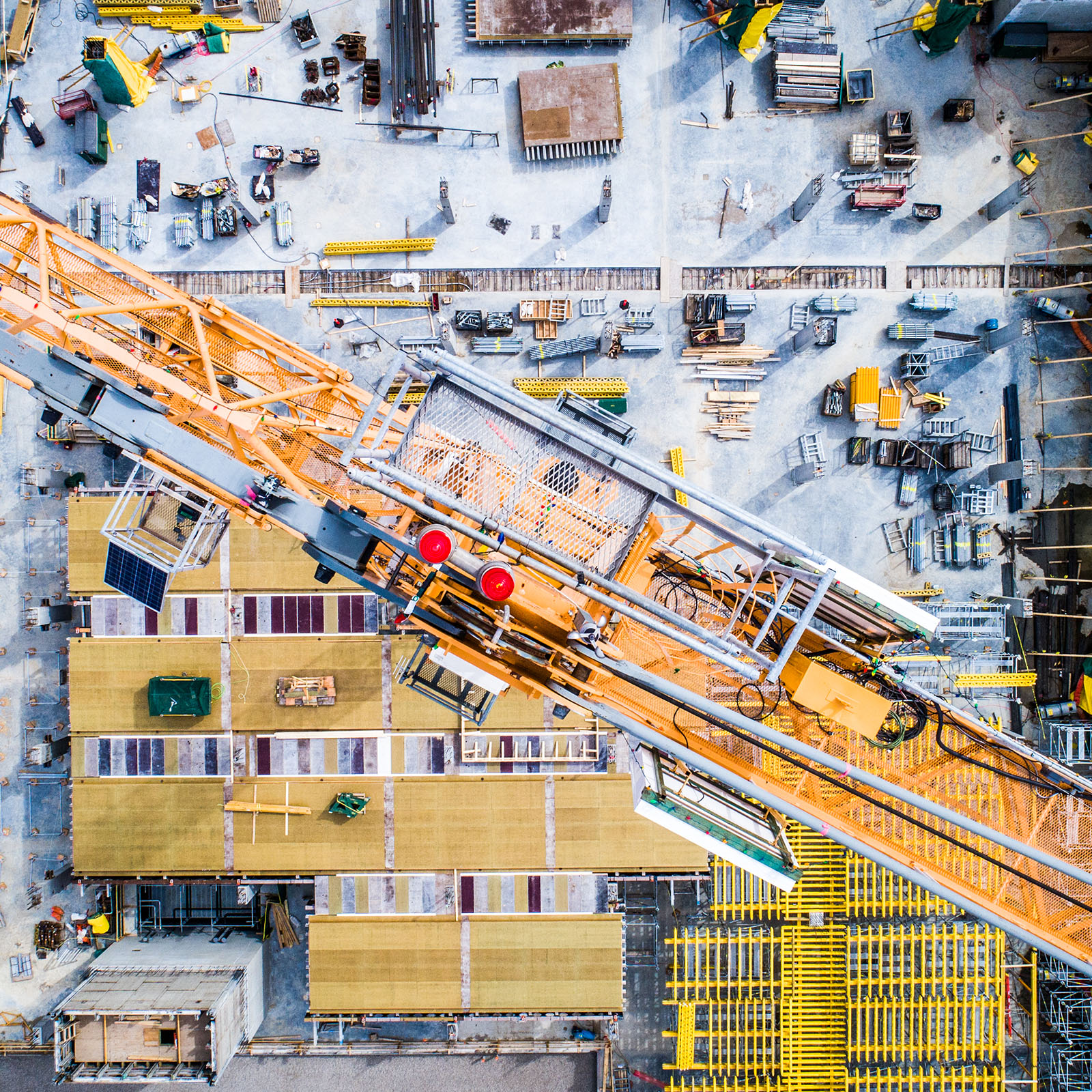Vue aérienne d'un chantier actif avec une grande grue jaune diagonale et divers matériaux de construction éparpillés en dessous.