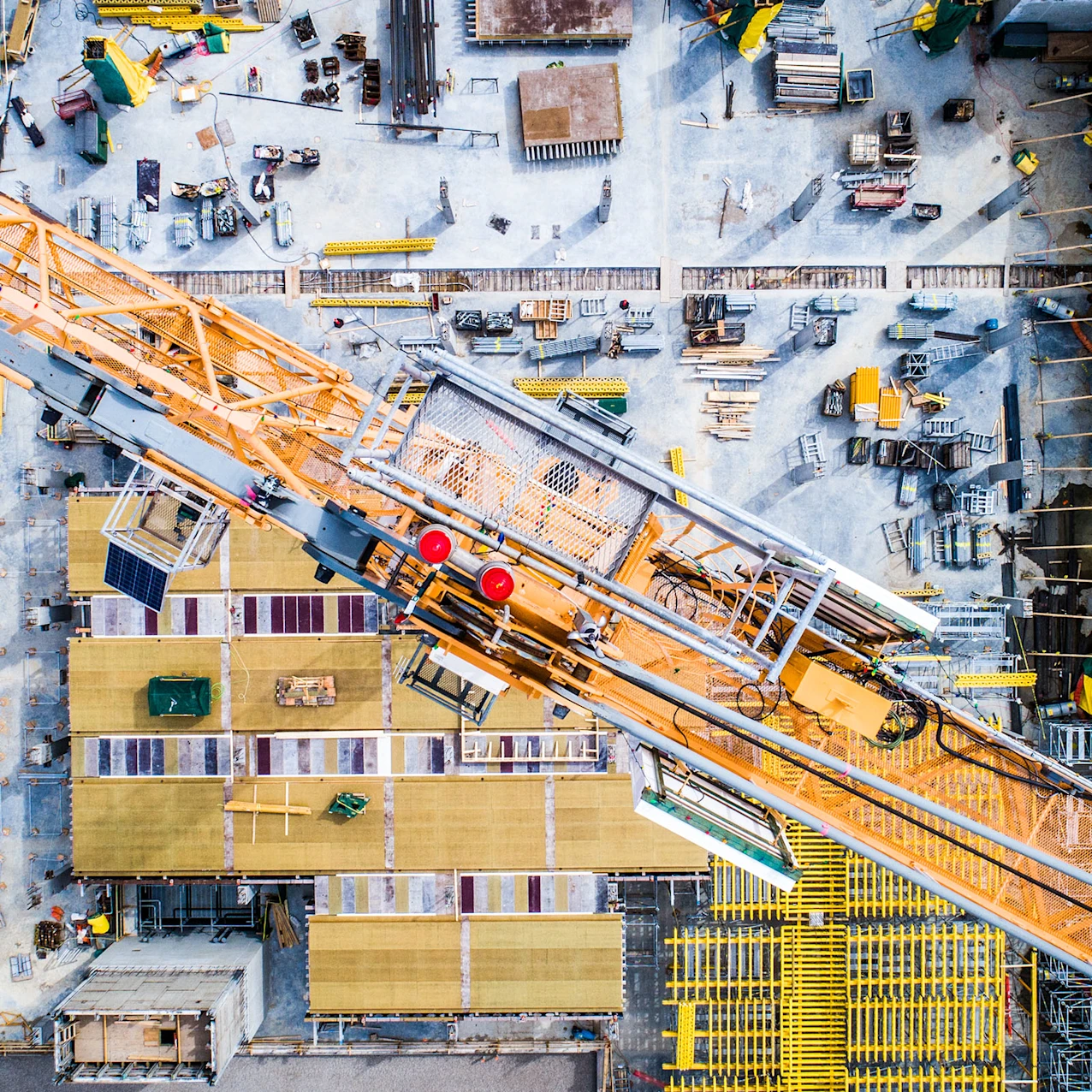 Vue aérienne d'un chantier actif avec une grande grue jaune diagonale et divers matériaux de construction éparpillés en dessous.