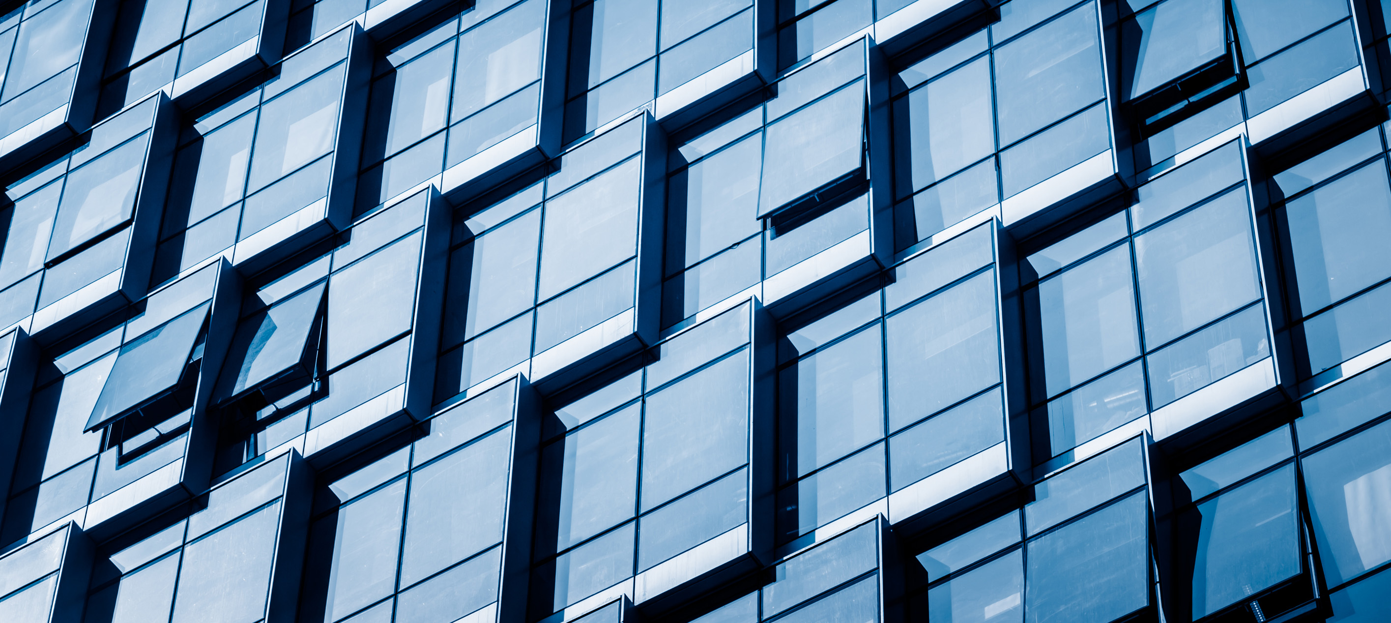 Close-up of a modern office building façade with reflective blue glass windows, several of which are partially open.