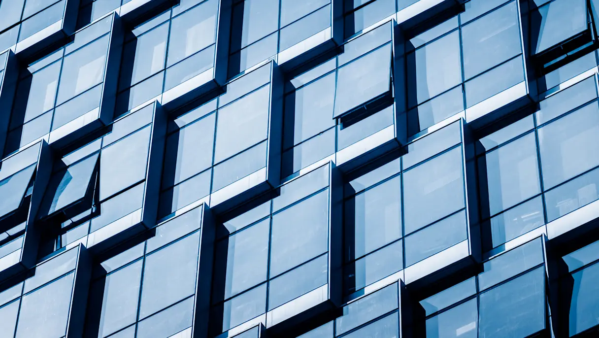 Close-up of a modern office building façade with reflective blue glass windows, several of which are partially open.