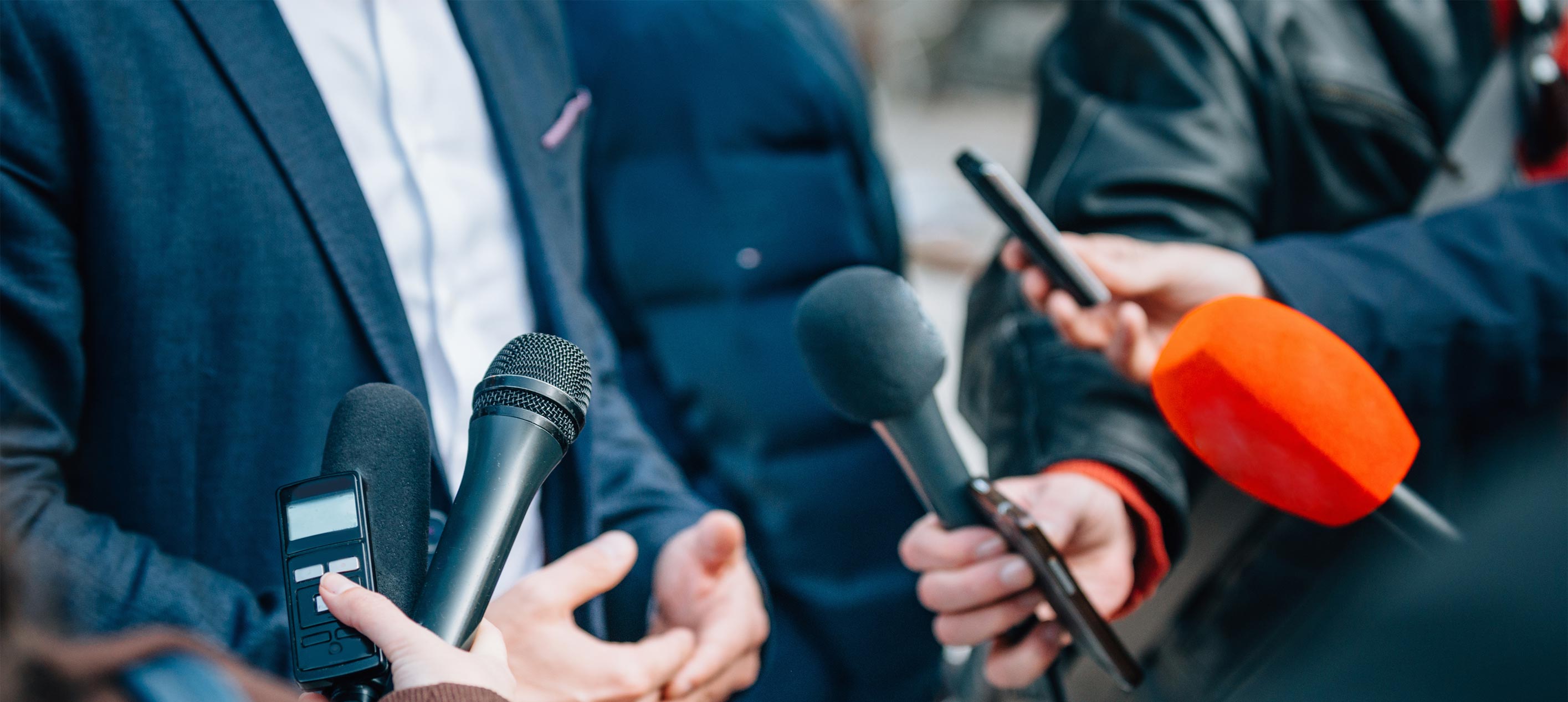 Reporters holding microphones in front of a person.