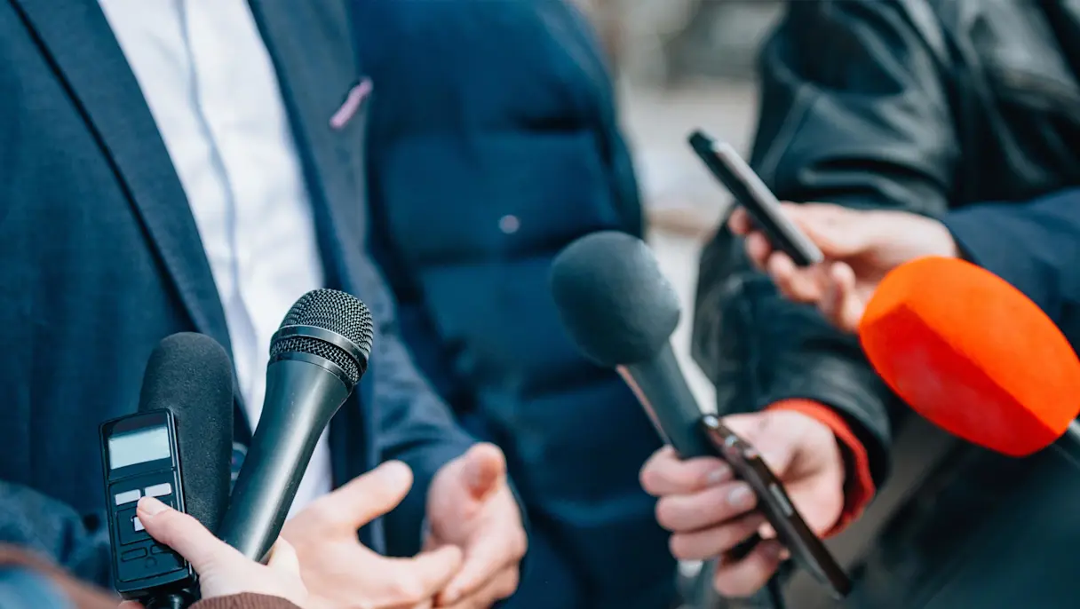 Reporters holding microphones in front of a person.