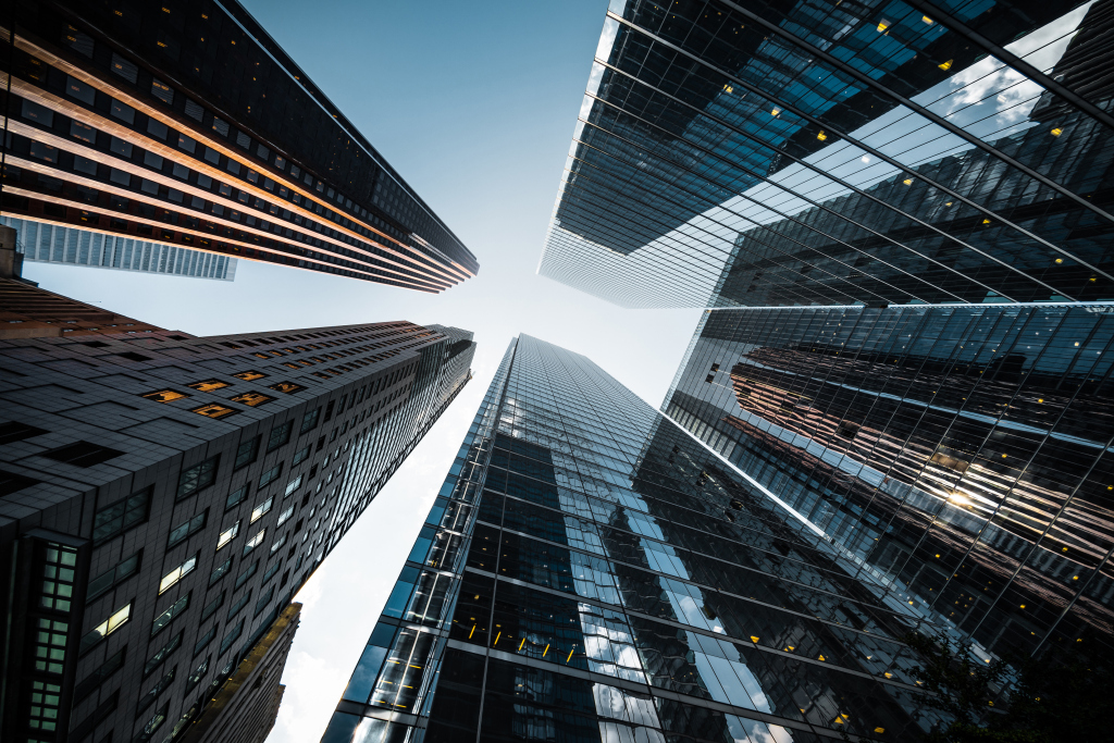 View looking up at several tall modern skyscrapers with glass and steel facades against a clear sky during daytime.