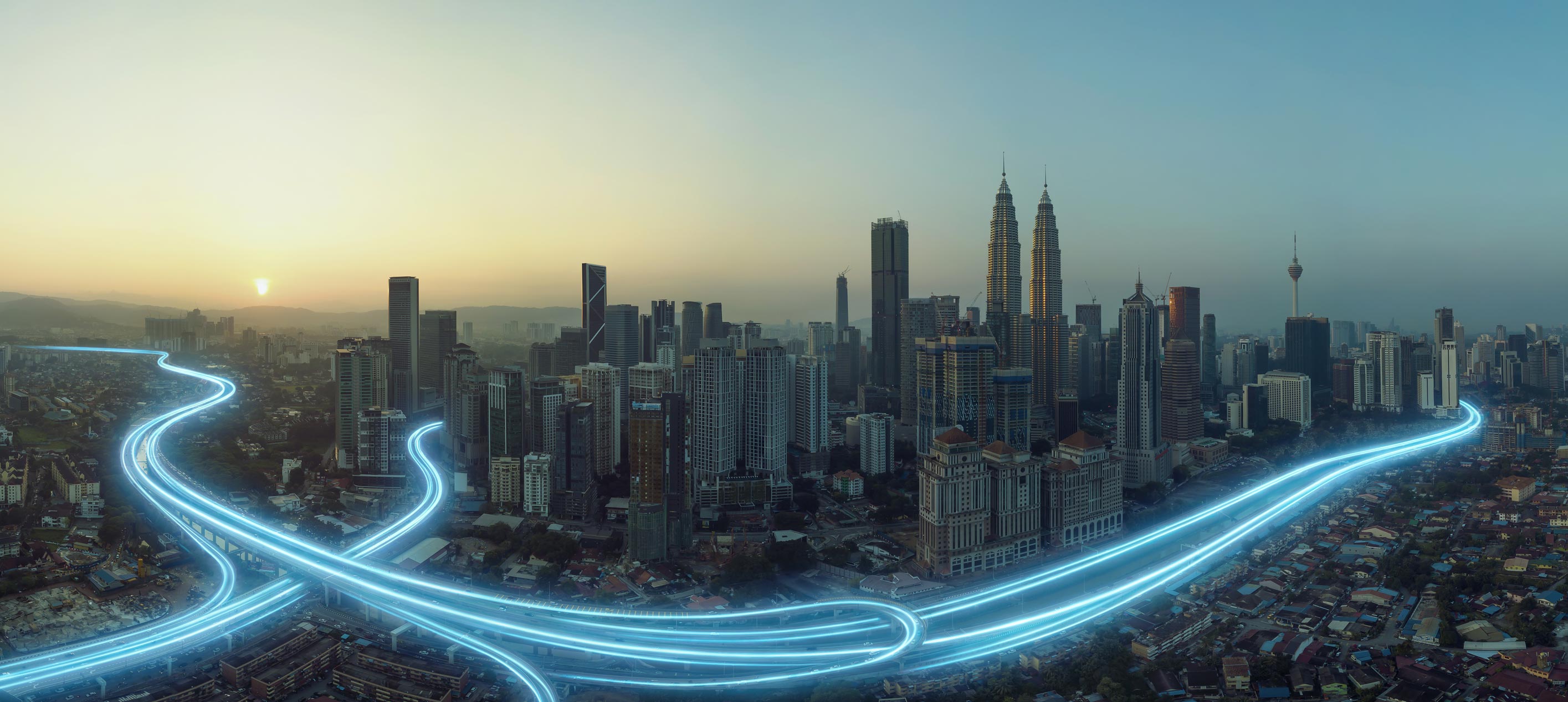 City skyline at sunset with glowing highway light trails.