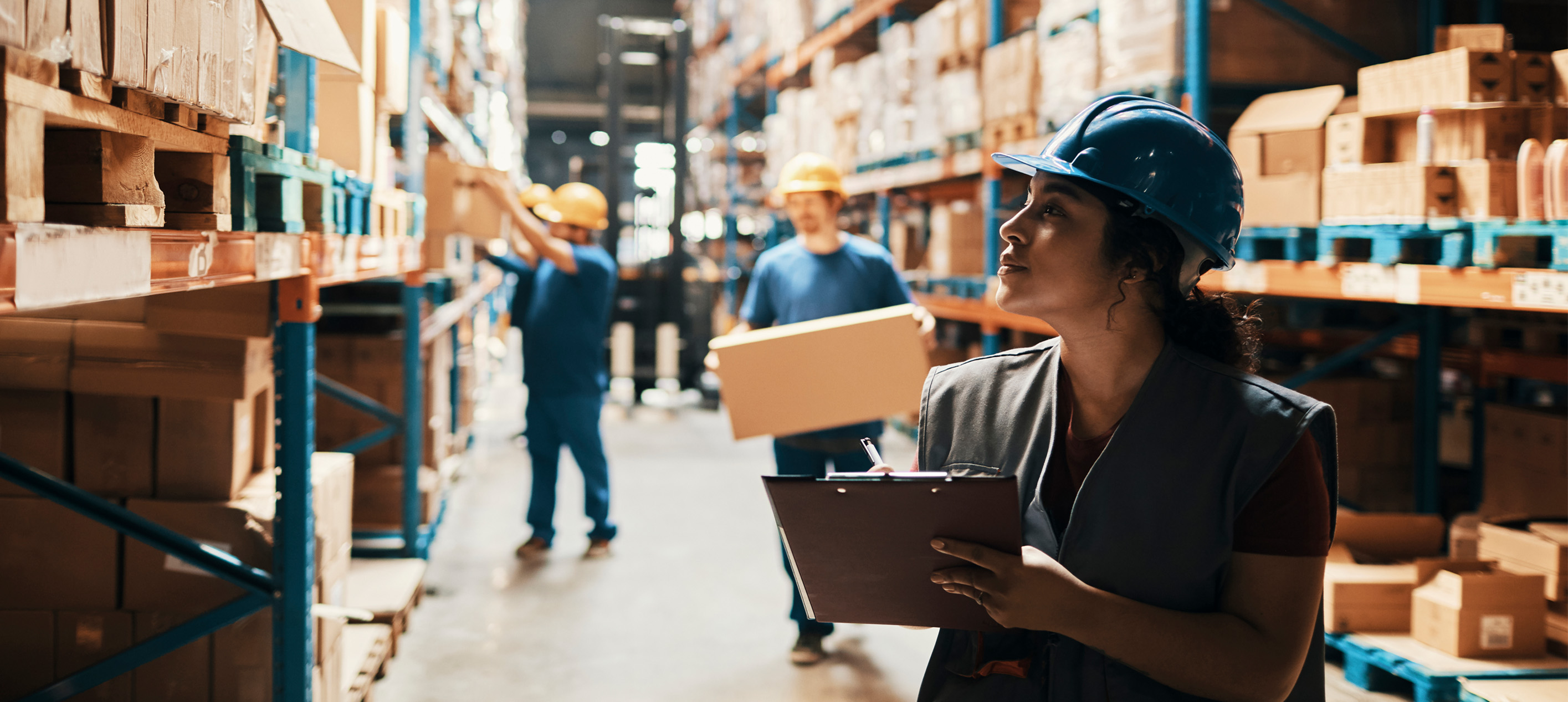 Warehouse worker using a tablet to manage inventory in a warehouse stocked with boxes and merchandise on shelves.