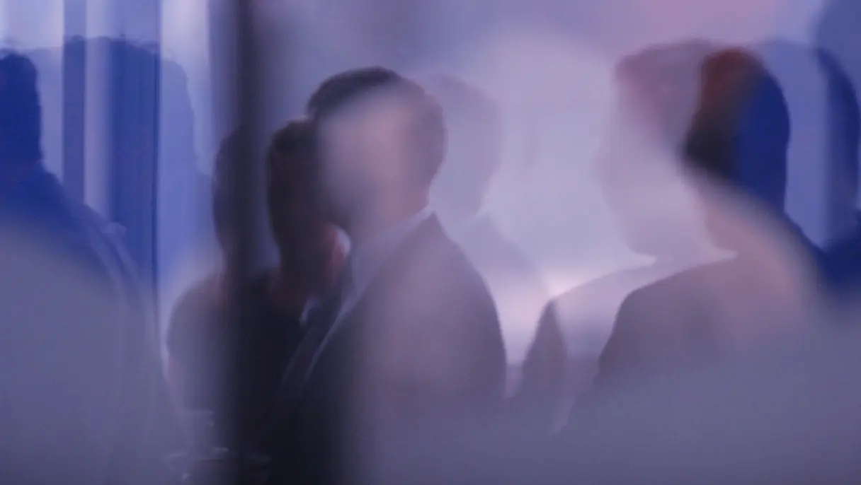 Blurry silhouettes of people standing in a room with soft blue and purple lighting, creating an indistinct group scene.