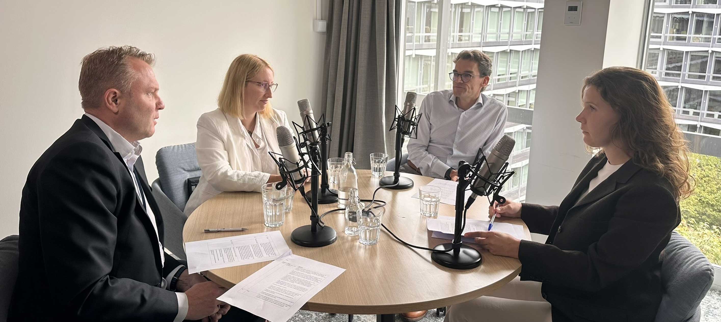 Four people discuss documents around a table with microphones.