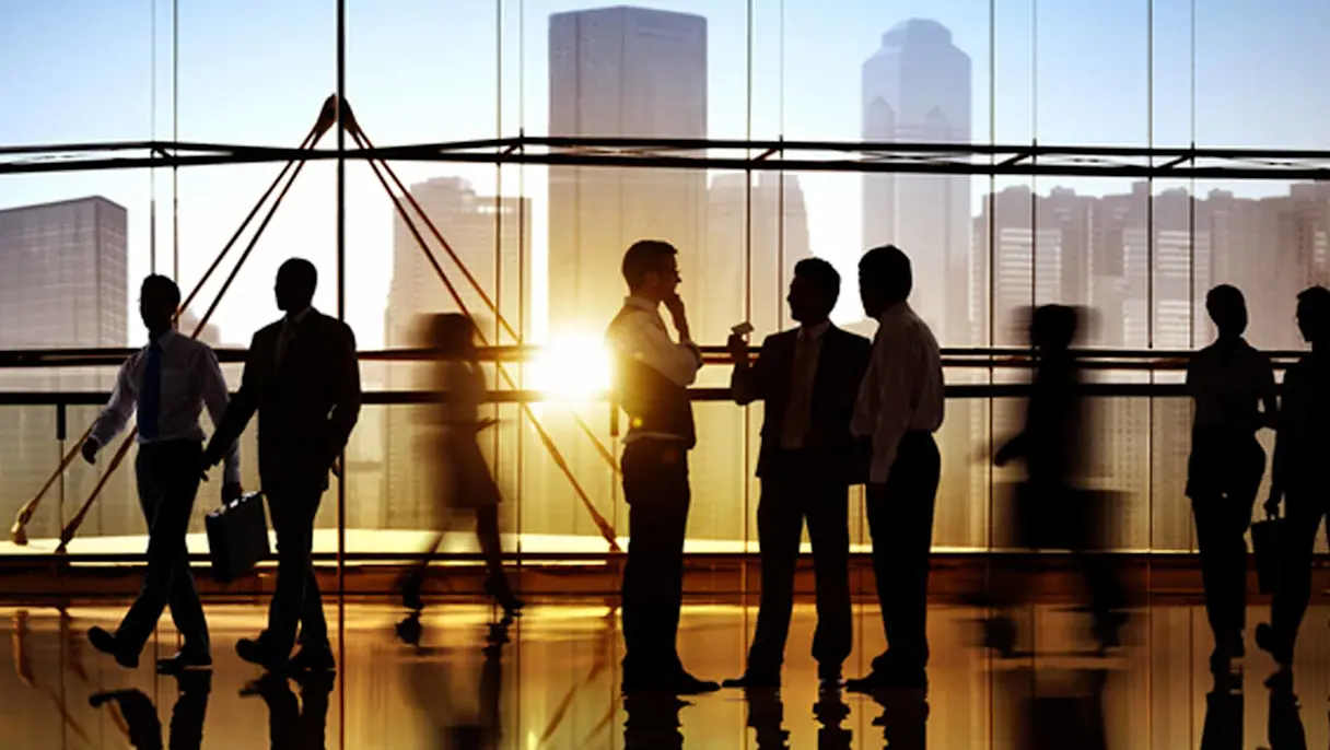 Business professionals silhouetted in a city office at sunset.