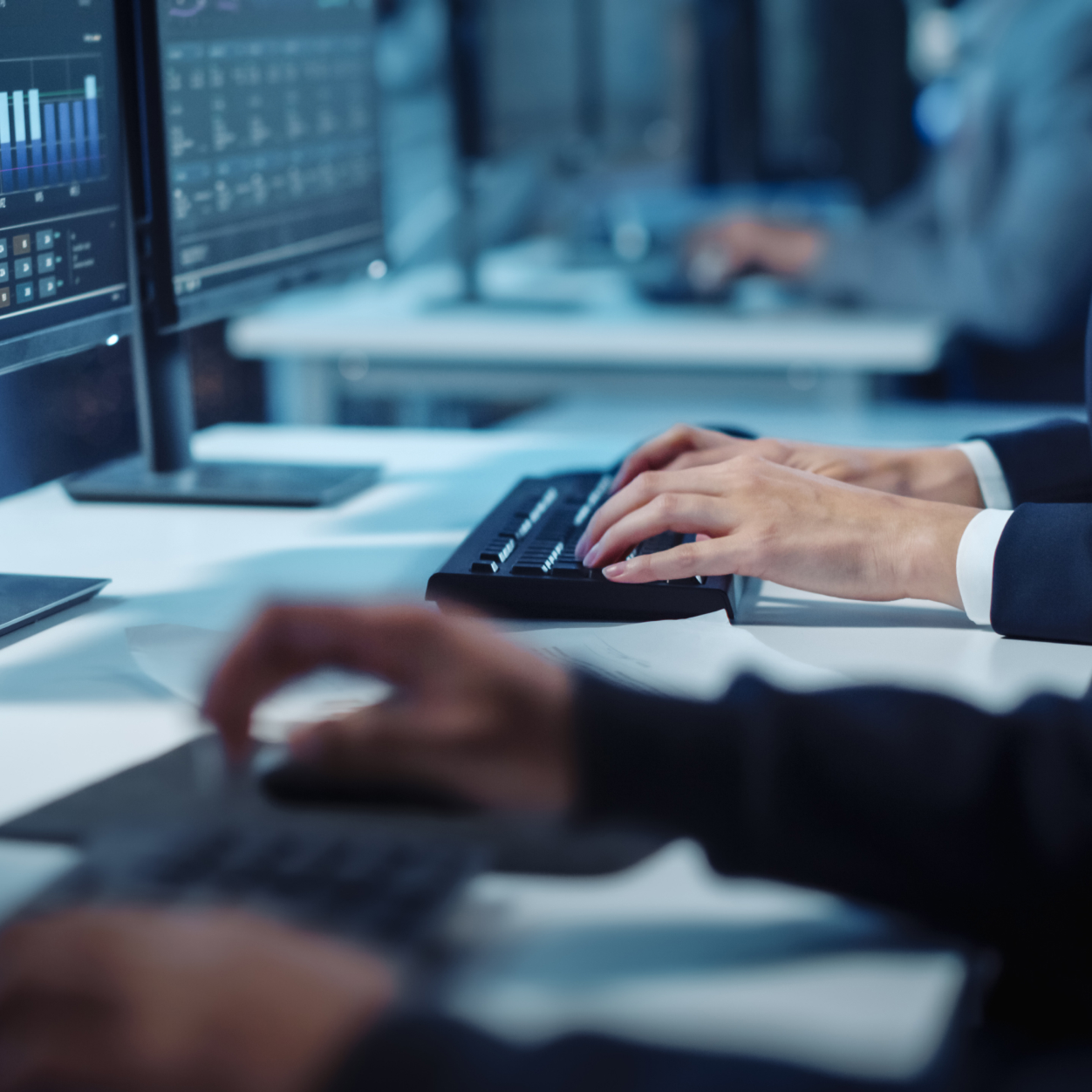 Close-up hands shot of a technical support specialist or software engineer working on a computer in a dark monitoring and control room.