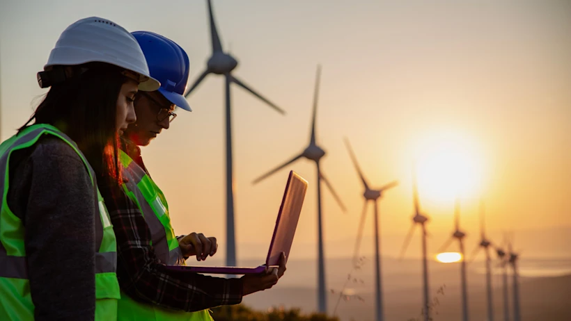 Field workers looking at a computer in a windmill field