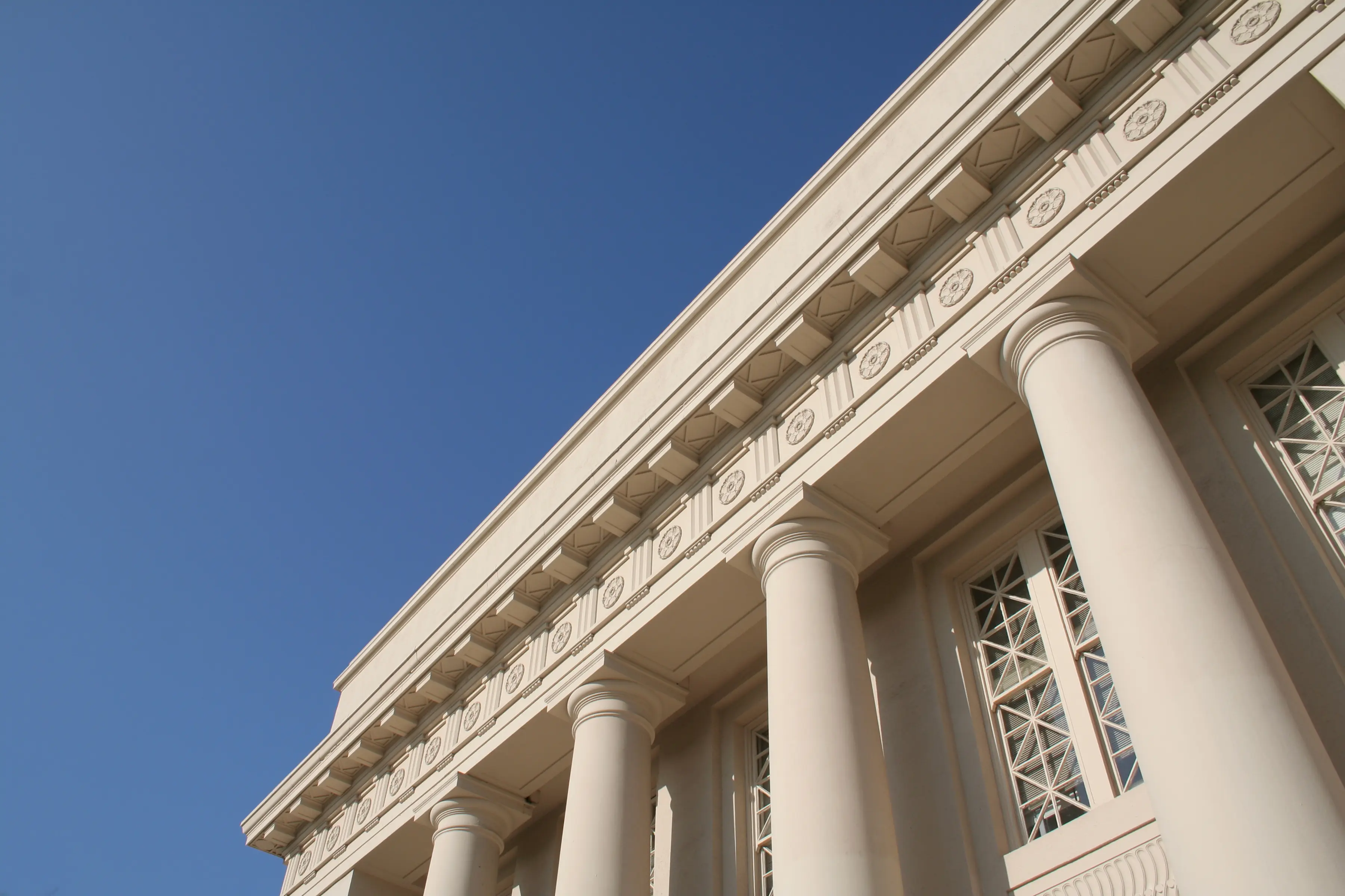 White neoclassical building facade with columns and ornate cornice, photographed from below against a blue sky.