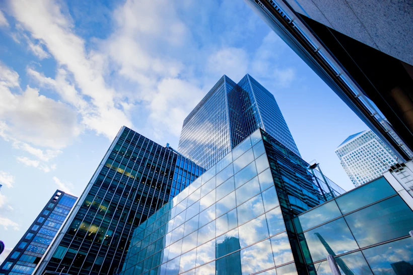 View looking up at several modern glass skyscrapers reflecting a partly cloudy blue sky.
