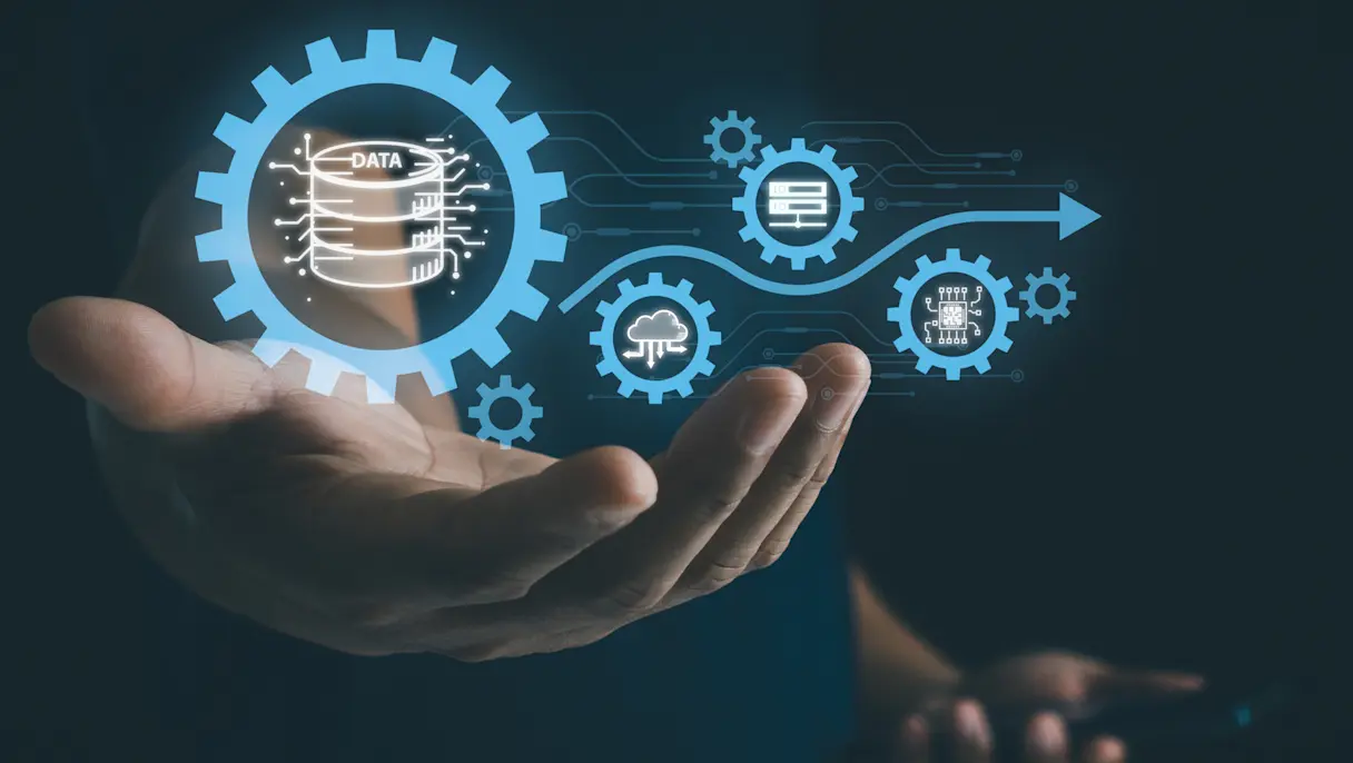 Hands held open with glowing blue gears and digital icons including a data stack, cloud and circuit board connected by a blue arrow.