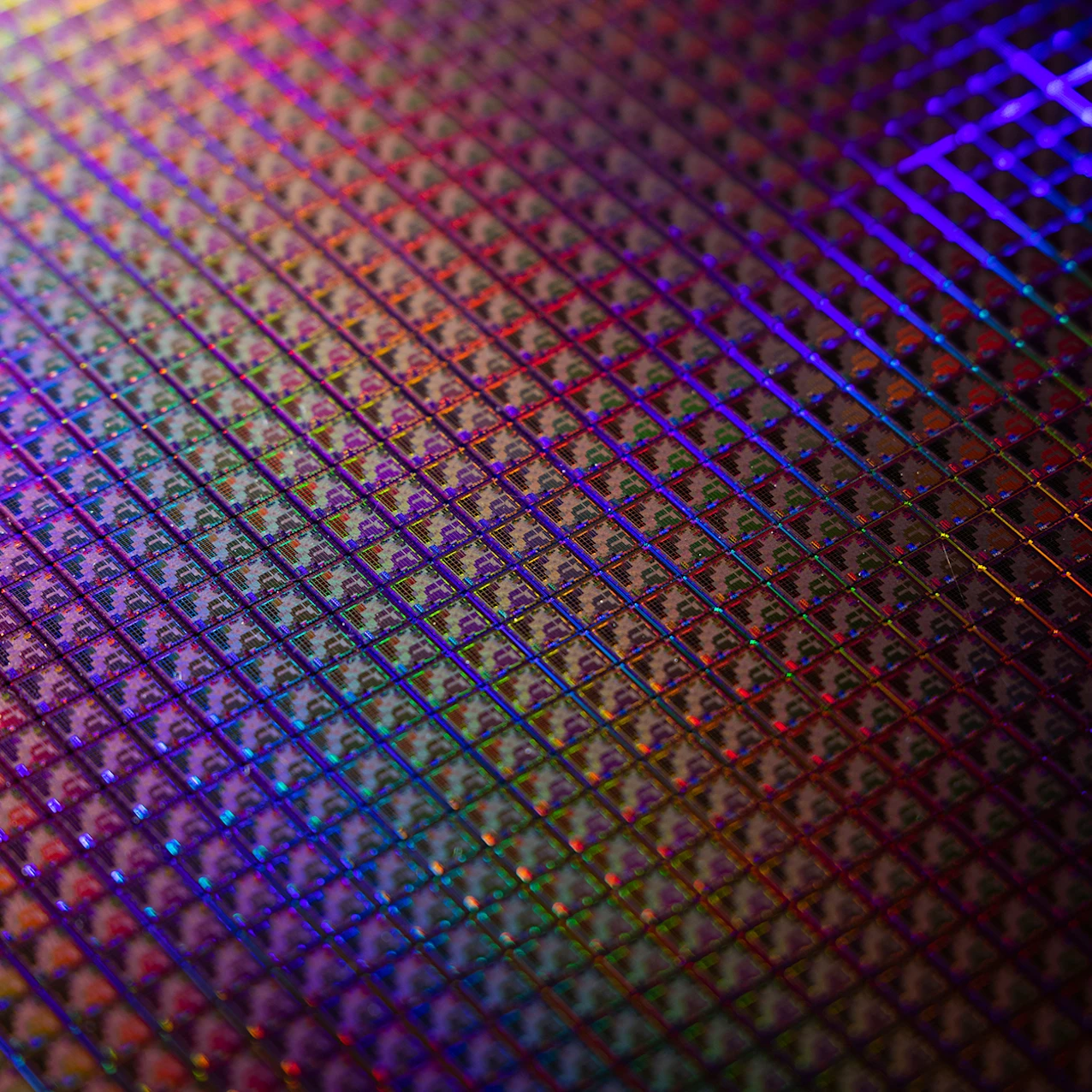 Close-up of a semiconductor wafer with intricate microchip patterns reflecting vibrant rainbow colors under bright light.