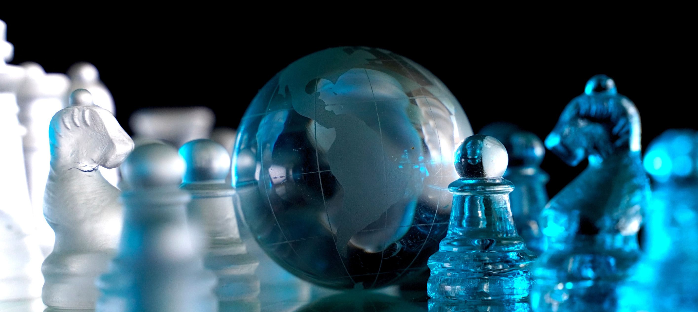 glass globe of the Earth positioned among glass chess pieces on a chessboard