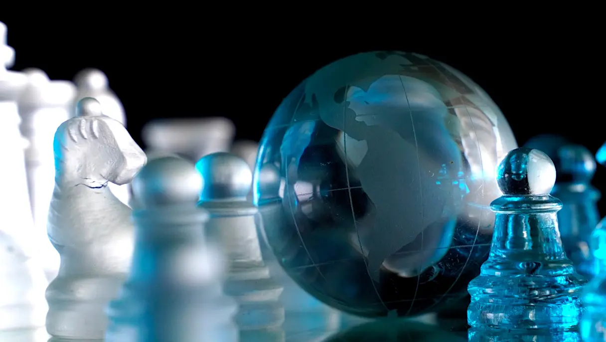 glass globe of the Earth positioned among glass chess pieces on a chessboard