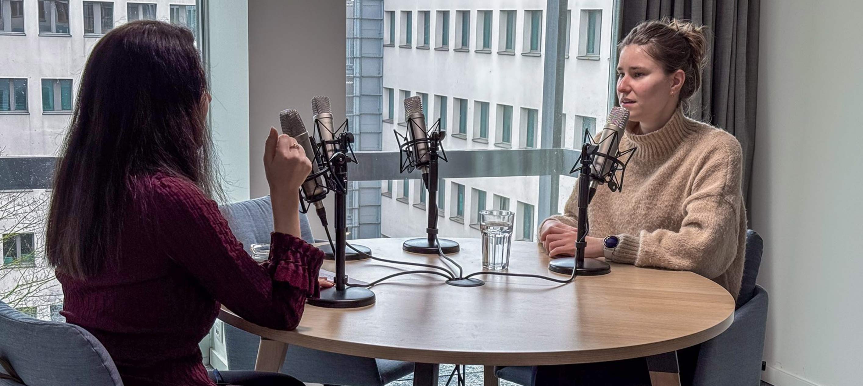Two professionals sitting across from each other with podcast mics in front of them