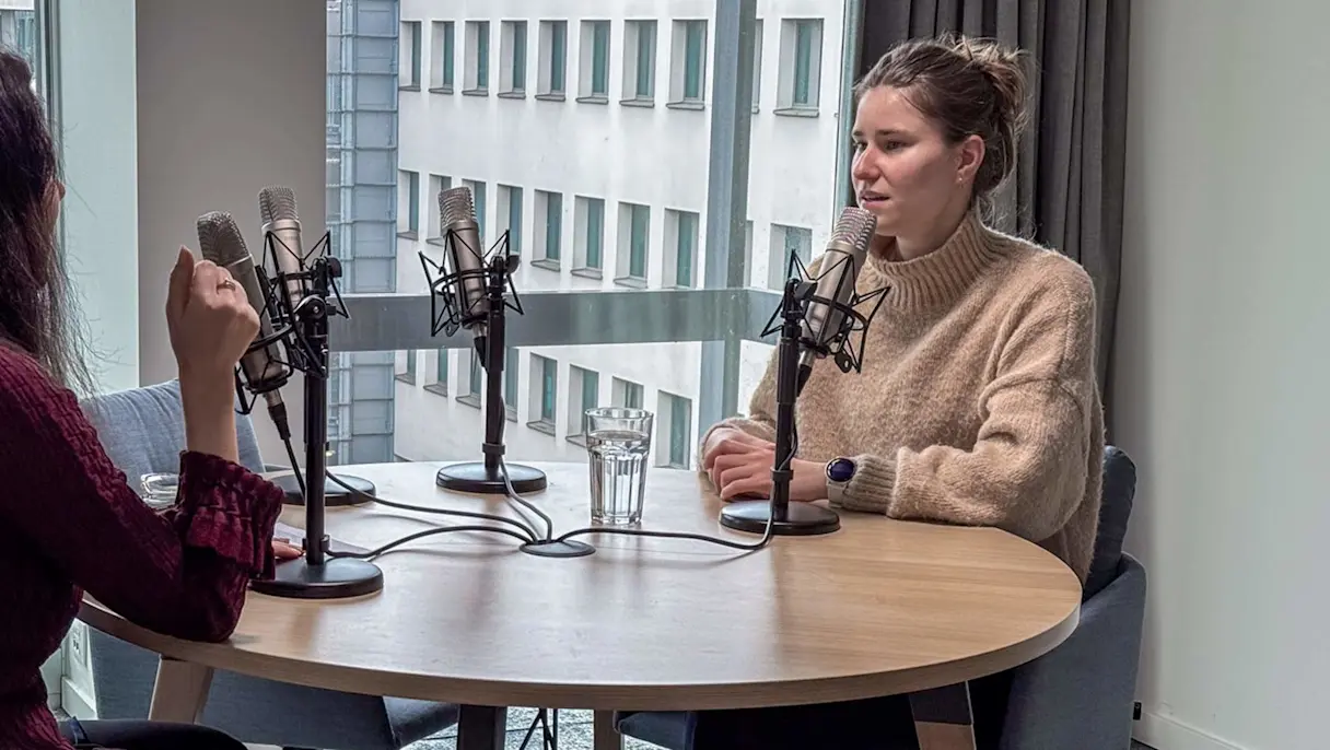 Two professionals sitting across from each other with podcast mics in front of them