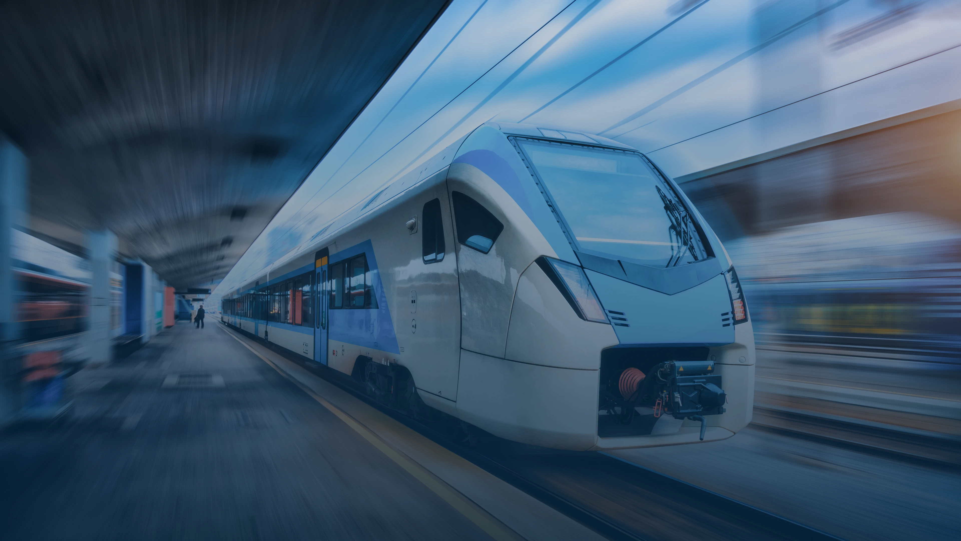 Modern white and blue passenger train at a station platform with motion blur effect, suggesting high speed or departure.