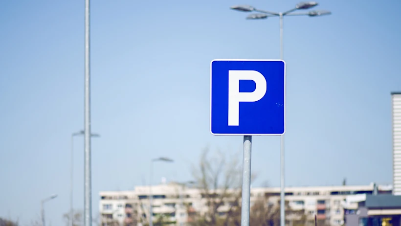 Blue parking sign with a white letter P on a pole, set against a clear sky and blurred urban background.