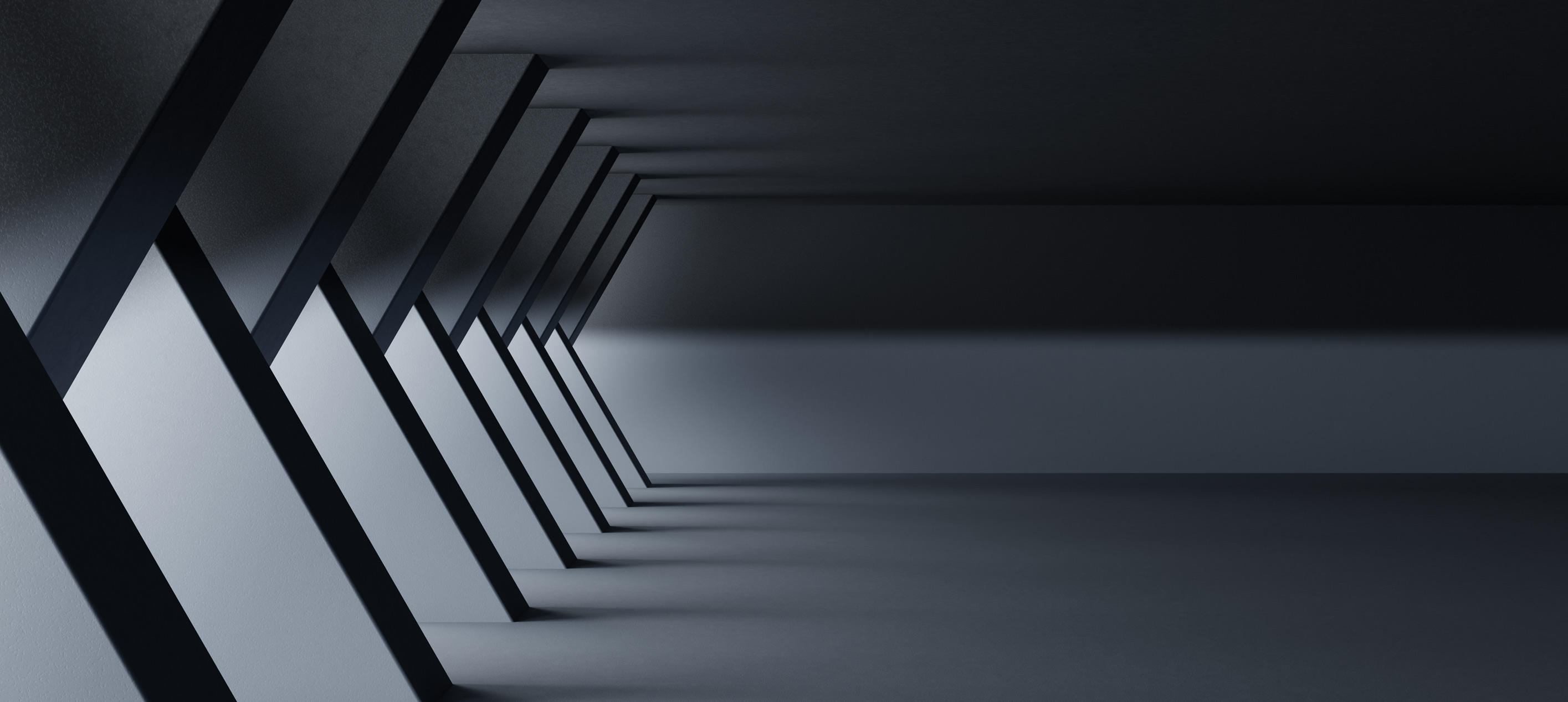 Dark grey hallway with a row of slanted columns along the left wall and soft light falling across a smooth floor.