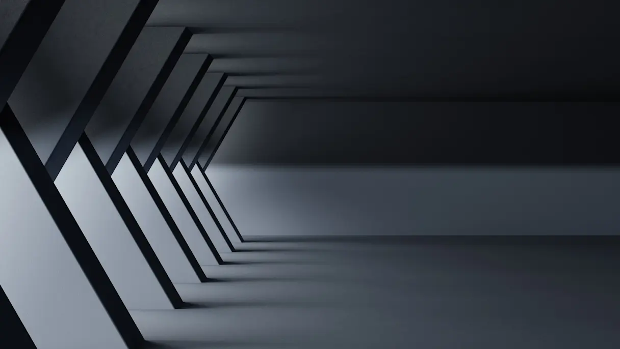 Dark grey hallway with a row of slanted columns along the left wall and soft light falling across a smooth floor.