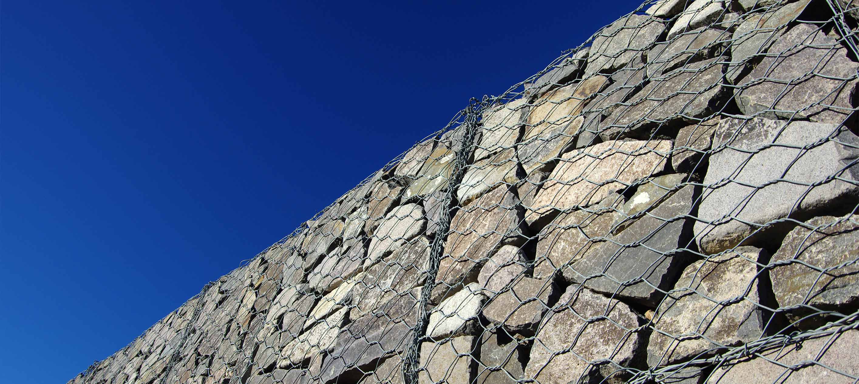 Stone Retaining Wall Encased in Wire Mesh Aginst a Clear Blue Sky