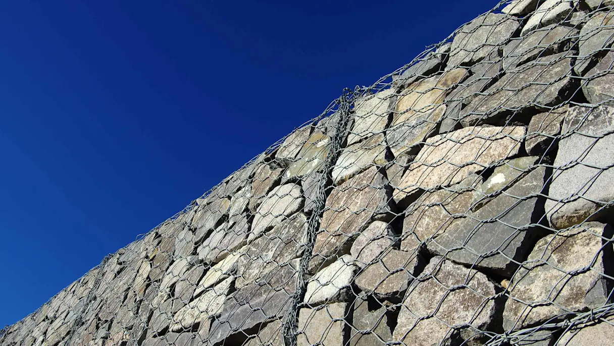 Stone Retaining Wall Encased in Wire Mesh Aginst a Clear Blue Sky