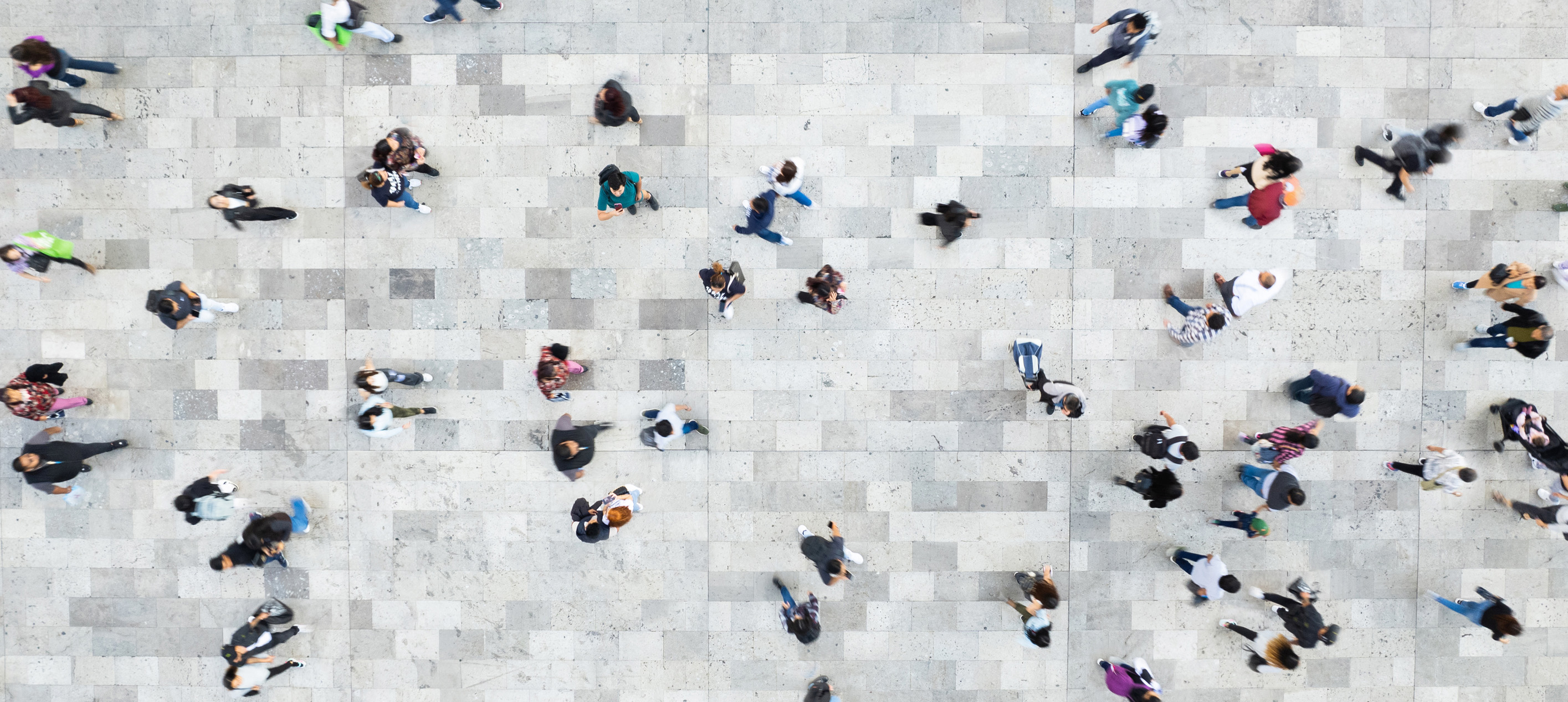 Overhead view of a diverse crowd of people walking across a large tiled public space