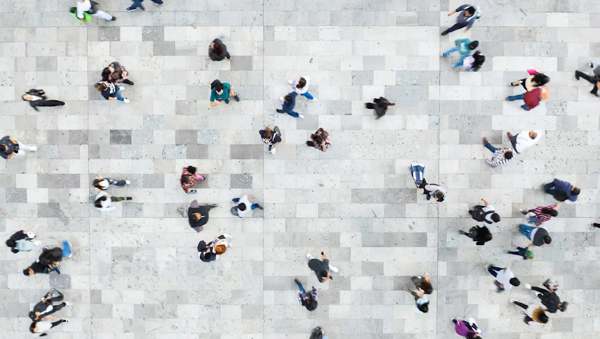 Overhead view of a diverse crowd of people walking across a large tiled public space