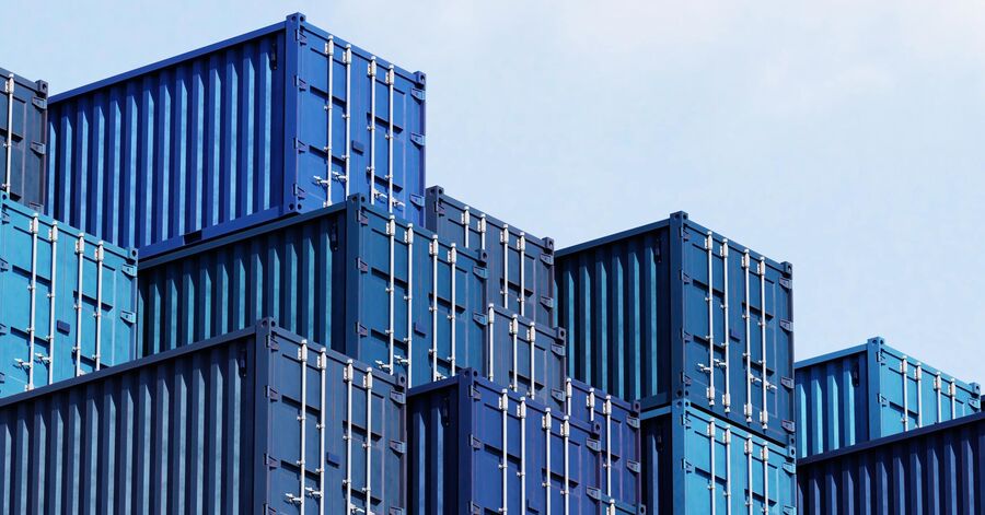 Stacked blue shipping containers arranged in rows against a clear sky.