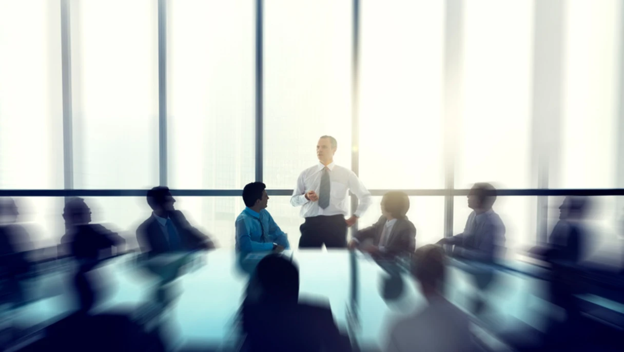A blurred image of a group of professionals sitting at a conference table