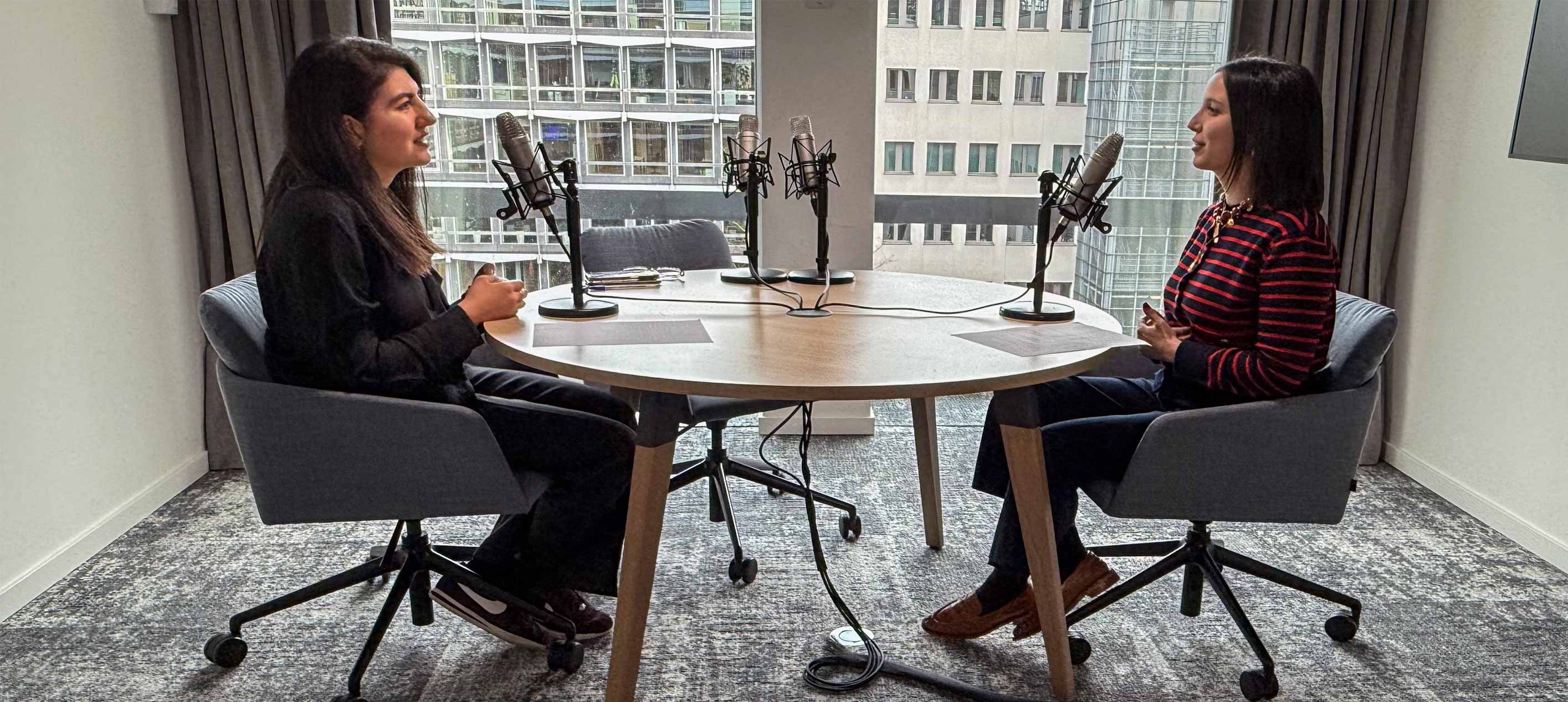 Two professionals sitting across from each other with podcast mics in front of them.