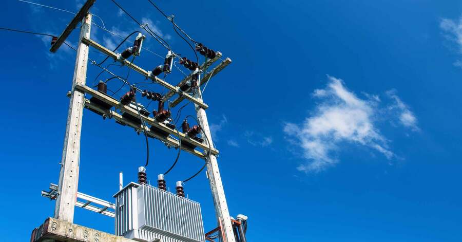 Electric power transformer and cables on utility pole against blue sky.