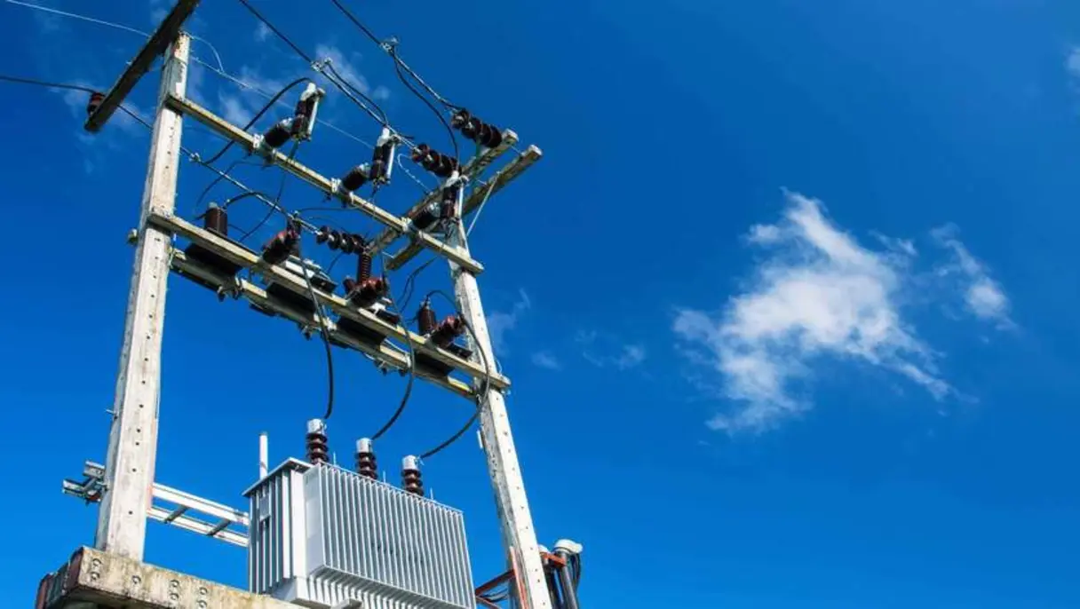 Electric power transformer and cables on utility pole against blue sky.
