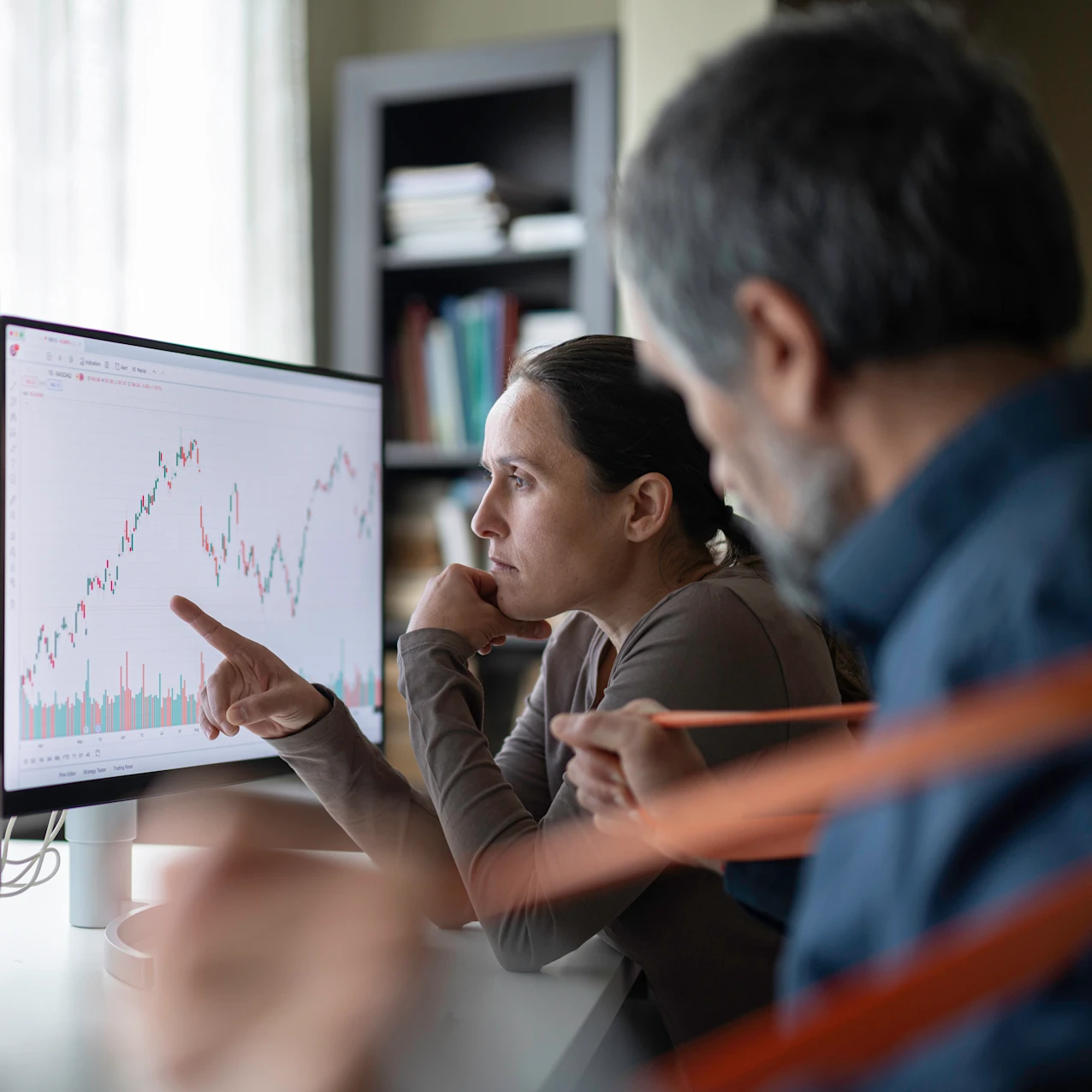 Two people analyzing stock market charts on dual computer monitors in a modern office setting.