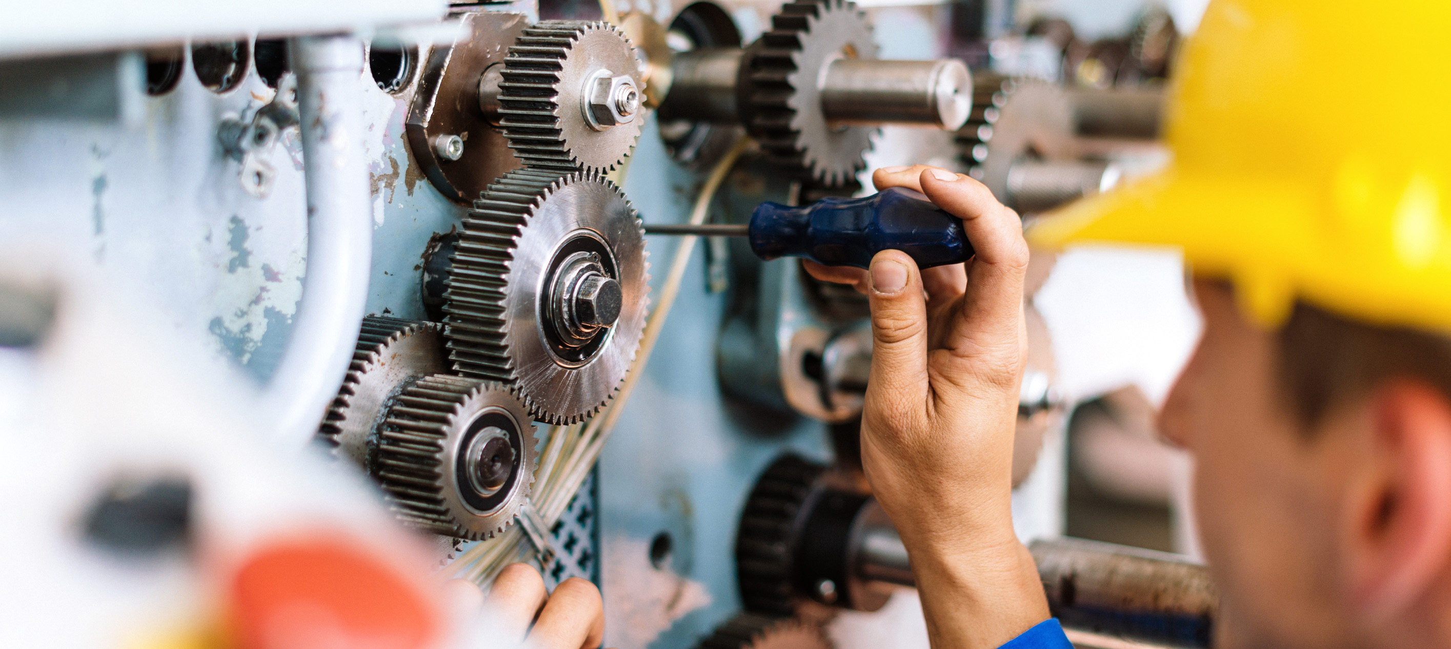 Industrial worker using a screwdriver to perform maintenance on gears and machinery in a manufacturing facility.