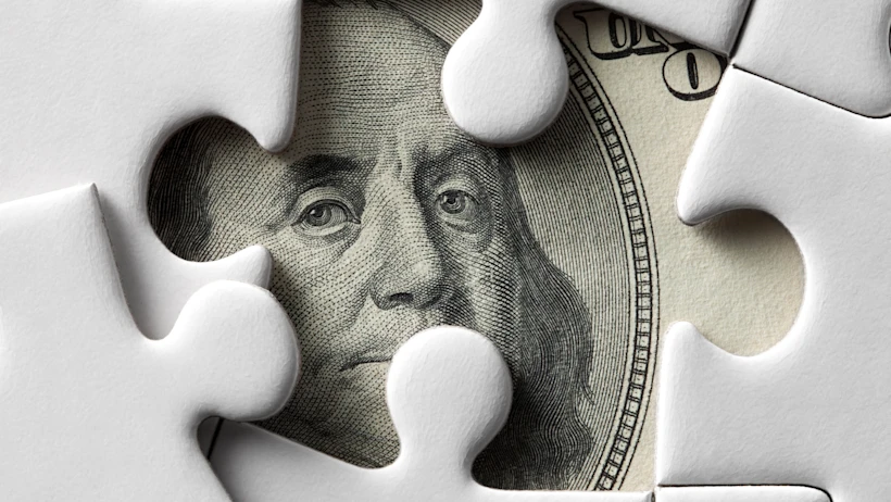 One Dollar note behind pieces of a puzzle