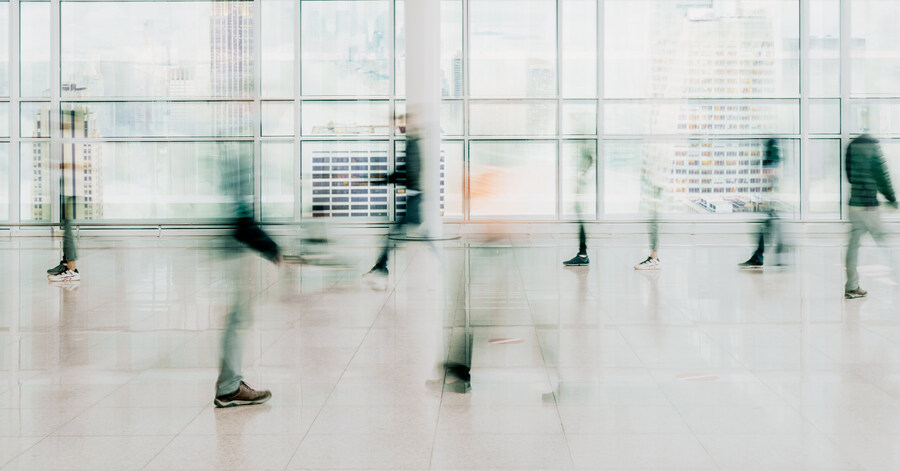 Blurred motion of people walking in a modern glass-walled building, conveying movement and a fast-paced business environment.
