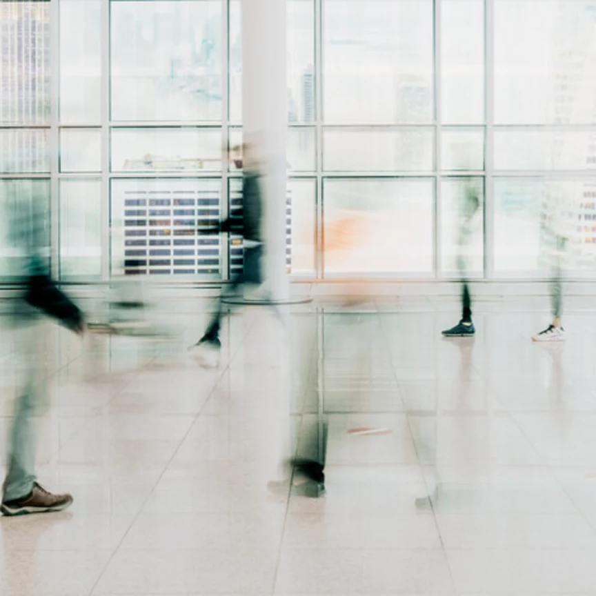 Blurred motion of people walking in a modern glass-walled building, conveying movement and a fast-paced business environment.