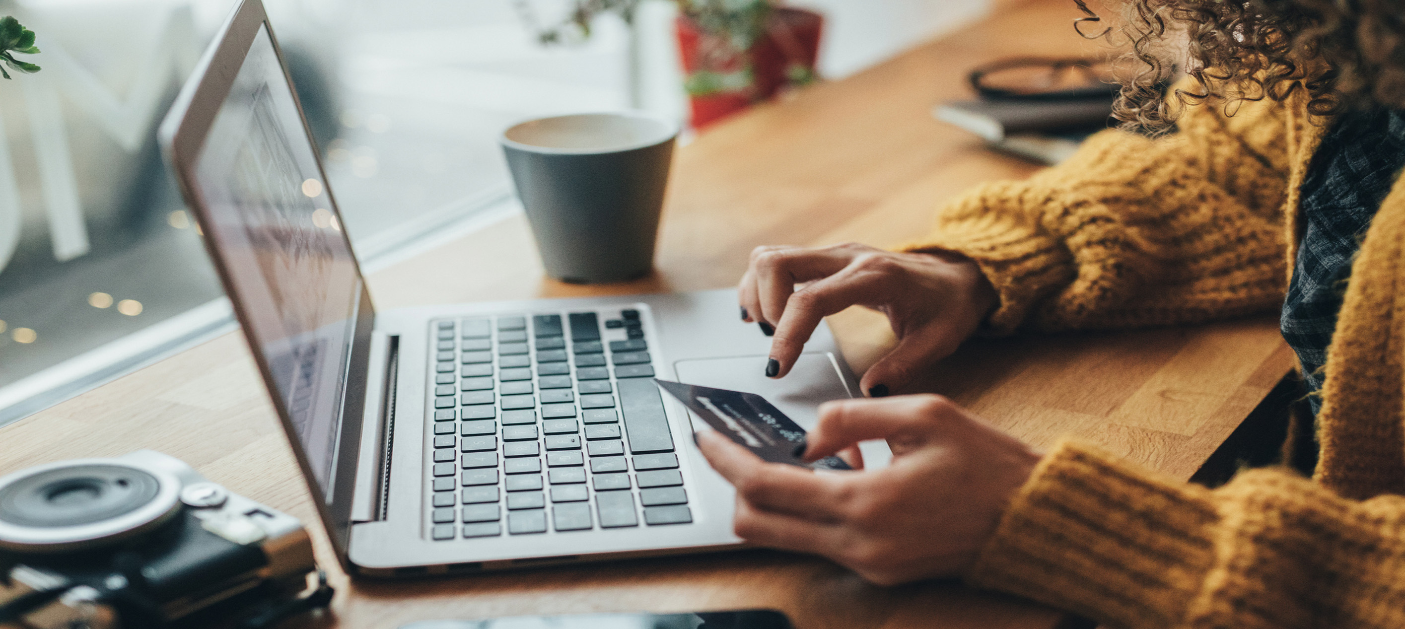 Women holding a credit card while typing numbers into a laptop computer.