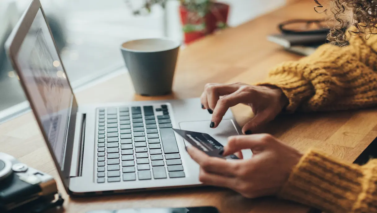 Women holding a credit card while typing numbers into a laptop computer.