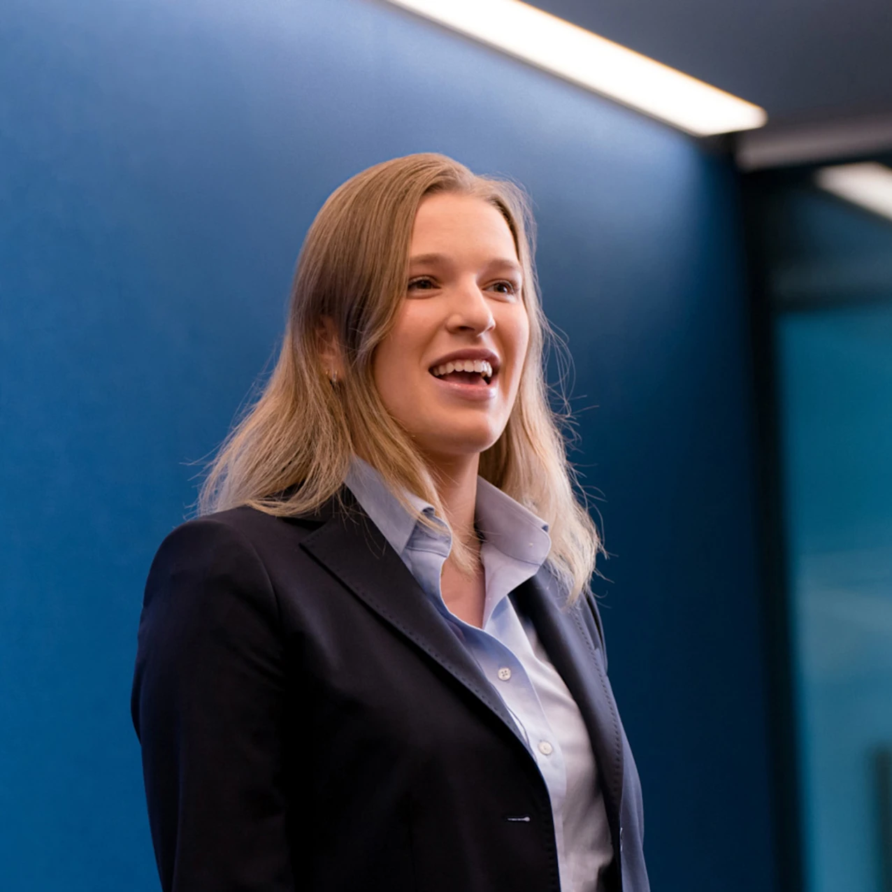 Woman in dark blue blazer addressing room cheerfully
